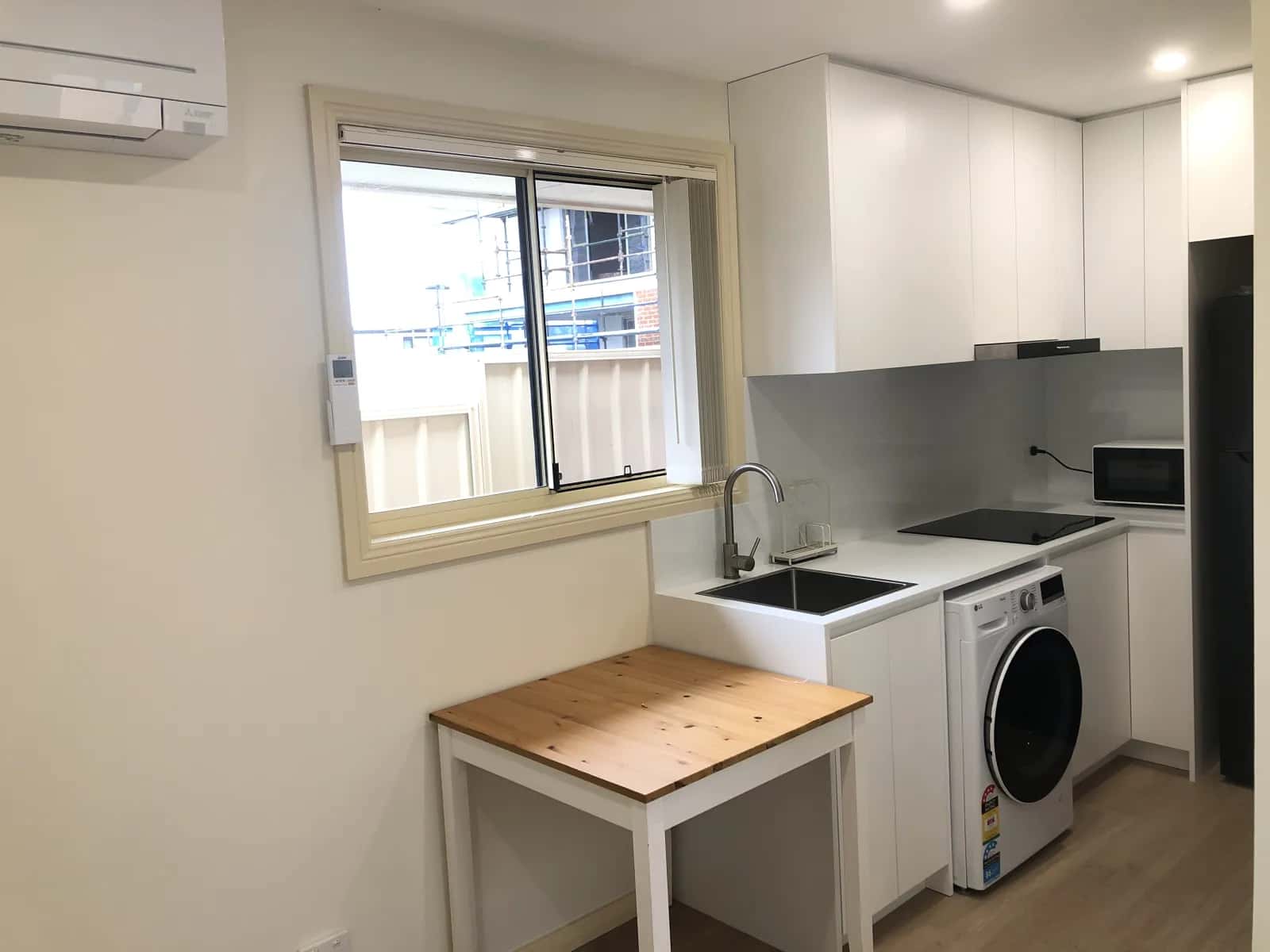 Completed Eastwood kitchenette with white cabinetry, black sink, glass splashback and laundry appliance